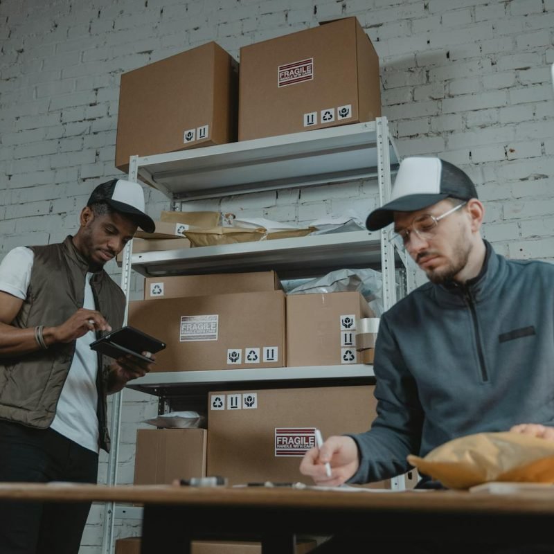 Two warehouse employees organizing and packing parcels for delivery in a modern indoor setting.